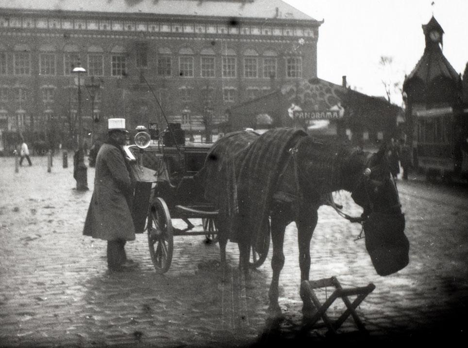 Hyrekusken her på Rådhuspladsen i København medbragte en sammenklappelig buk, som hesten kunne bruge, når den fik muleposen. Foto: Paul Fischer, Københavns Museum, kbhbilleder.dk