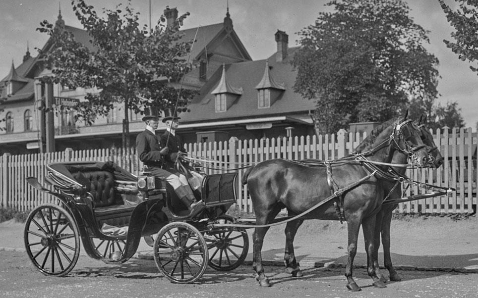 Direktør Carl Morescos uniformerede kusk og vogntjener kører i 1904 direktørens smukke Mylord forspændt to sorte vallakker fra Ungarn.