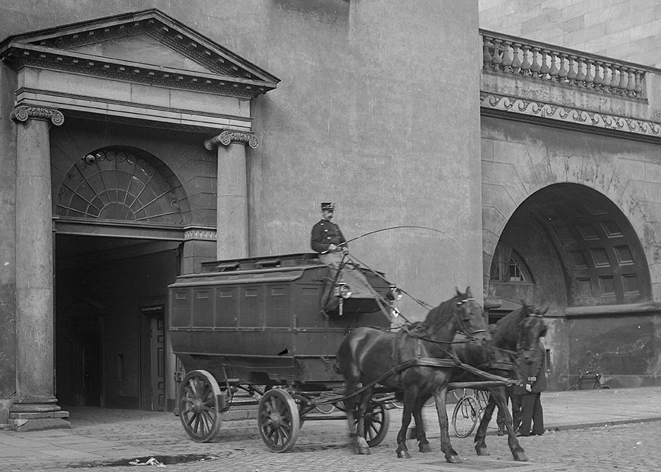 Fangevogn "Salatfadet" kører ud af porten ved Opdagelsespolitiet, Københavns domhus. Tospandet går med bringeseler. Foto: Lars Peter Elfelt, 1904, Det kgl. Biblioteks billedsamling.