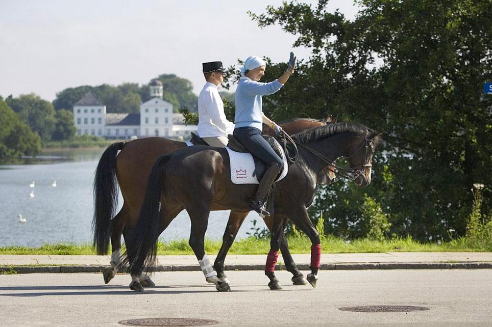 H.K.H. Prinsesse Benedikte på hesten Don Giovan, der er af egen avl, i selskab med biløber Ole Mortensen med Gråsten Slot i baggrunden. Billedet blev bragt i Christina Hauschildts og Eva Nitschkes bog 'De kongelige Heste' fra 2008. Foto: Christina Hauschildt ©